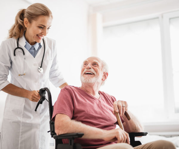 Old bearded man sitting in wheelchair while doctor standing behind